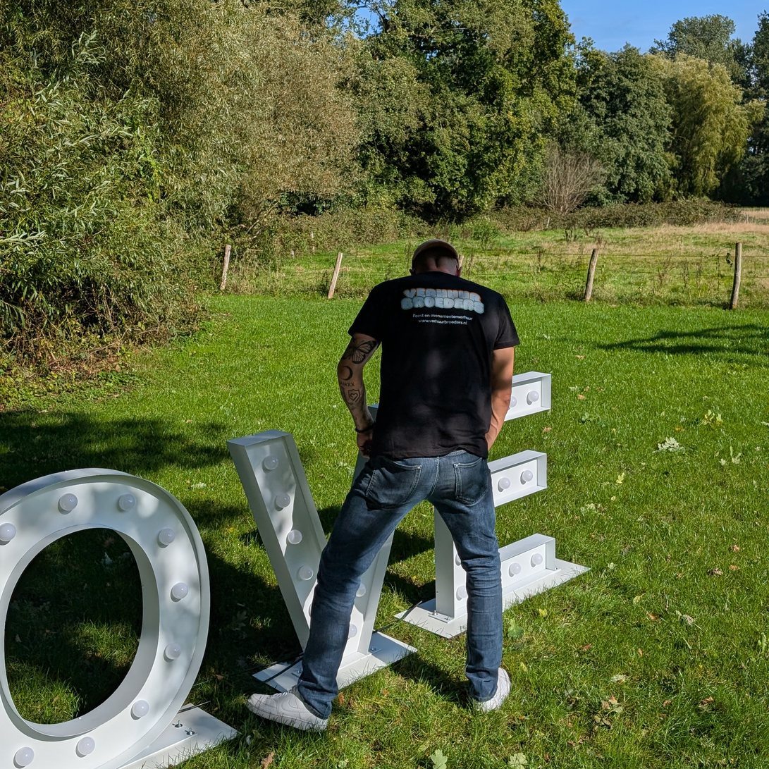 Frank naast de LOVE lichtletters op een grasveld, geeft goed beeld van de schaal van een meter hoog